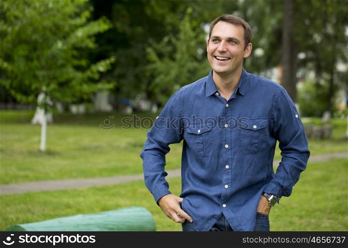 Portrait of a young handsome man in a blue shirt on the background of summer park