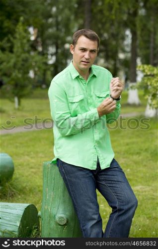 Portrait of a young handsome man in a green shirt on the background of summer park