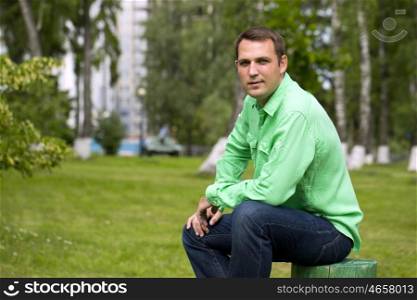 Portrait of a young handsome man in a green shirt on the background of summer park