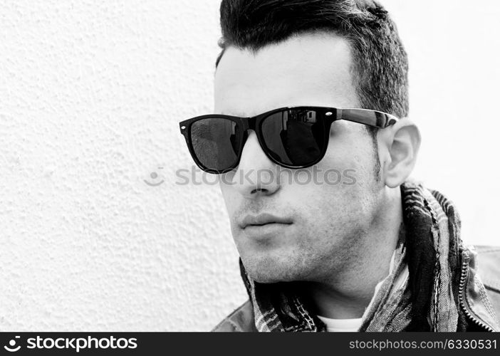 Portrait of a young handsome man, model of fashion, wearing tinted sunglasses in urban background