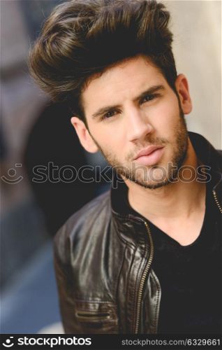 Portrait of a young handsome man, model of fashion, with modern hairstyle in urban background wearing and leather jacket