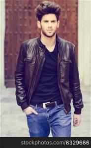 Portrait of a young handsome man, model of fashion, with modern hairstyle in urban background wearing blue jeans and leather jacket