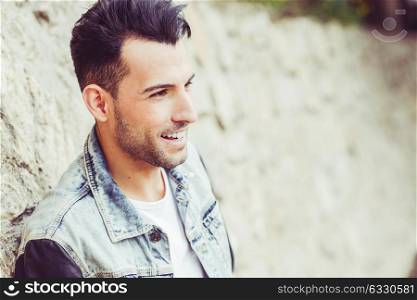 Portrait of a young handsome man, model of fashion, with modern hairstyle in urban background, smiling
