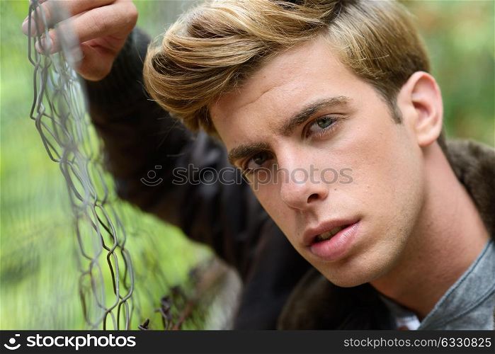 Portrait of a young handsome man, model of fashion, with modern hairstyle in urban background wearing aviator leather jacket. Blonde hair