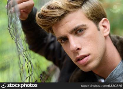 Portrait of a young handsome man, model of fashion, with modern hairstyle in urban background wearing aviator leather jacket. Blonde hair