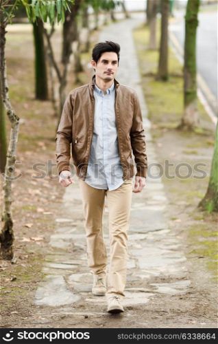 Portrait of a young handsome man, model of fashion, with modern hairstyle walking in urban background, wearing casual clothes.