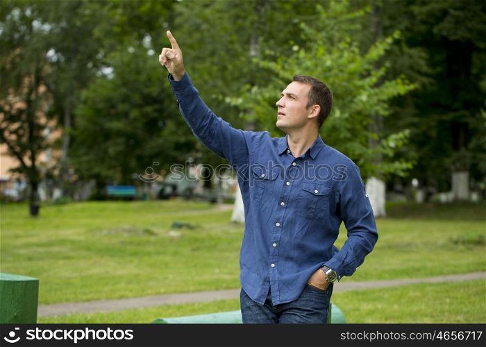 Portrait of a young handsome man points his finger to the side, on the background of summer park