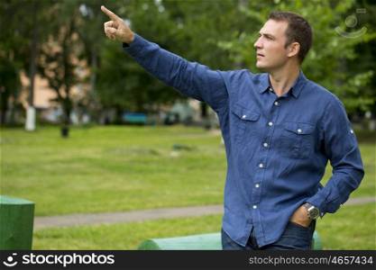 Portrait of a young handsome man points his finger to the side, on the background of summer park