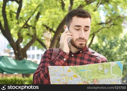 Portrait of a young handsome tourist man looking at a map and talking on phone. Tourism concept. Outdoors.