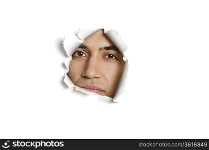 Portrait of a young Indian man peeking from ripped paper hole