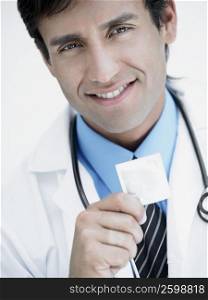 Portrait of a young male doctor smiling and holding a condom