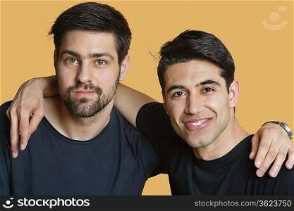 Portrait of a young male friends with arms around over colored background