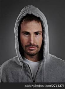 Portrait of a young male model wearing a gray hoodie and white t-shirt. He has a serious expression and is shot on a gray background.. Commercial Photography