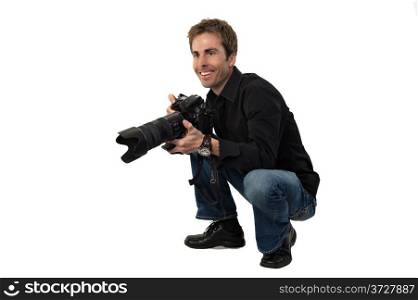 Portrait of a young male photographer with a professional camera, crouching down, getting ready to take pictures.