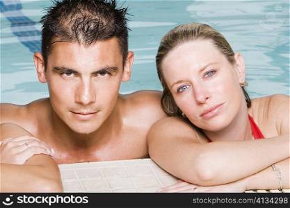 Portrait of a young man and a young woman leaning at the edge of a swimming pool