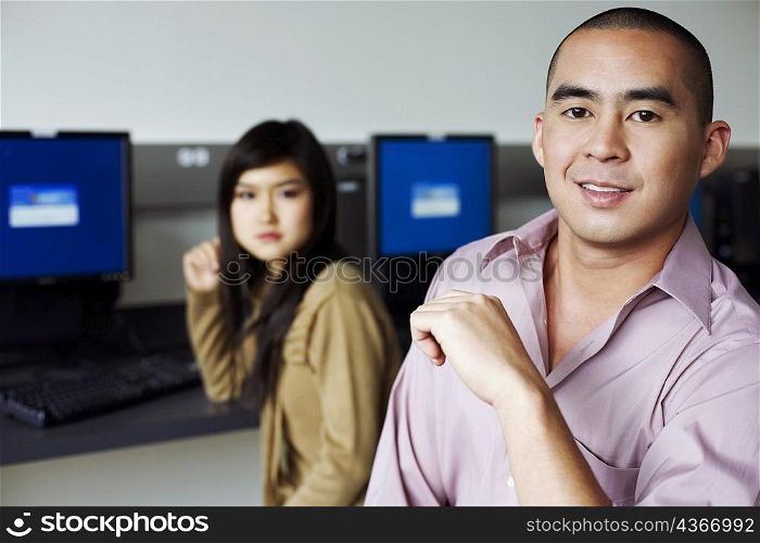 Portrait of a young man and a young woman sitting in front of computers and grinning