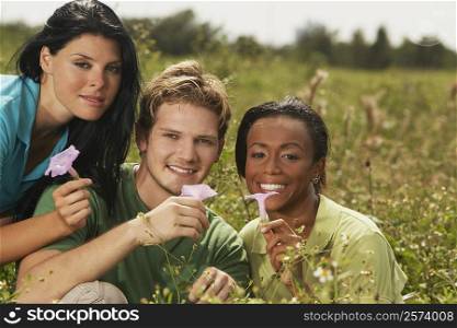 Portrait of a young man and two young women holding flowers