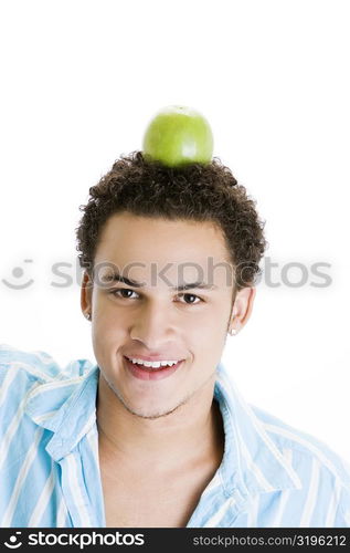 Portrait of a young man balancing a green apple on his head