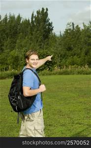 Portrait of a young man carrying a backpack pointing forward