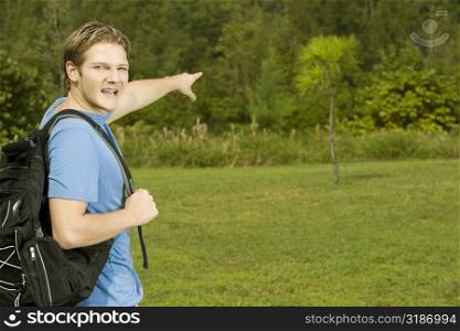 Portrait of a young man carrying a backpack pointing forward