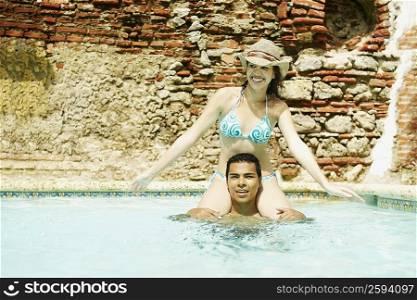 Portrait of a young man carrying a young woman on his shoulders in a swimming pool