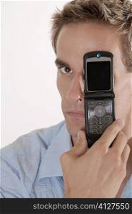 Portrait of a young man covering his eye with a mobile phone