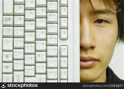 Portrait of a young man covering his face with a computer keyboard