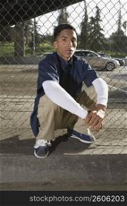 Portrait of a young man crouching in front of a chain-link fence