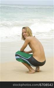 Portrait of a young man crouching on the beach and smiling