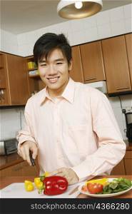 Portrait of a young man cutting vegetables at a kitchen counter