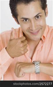 Portrait of a young man giving thumbs up after checking the time on his wristwatch