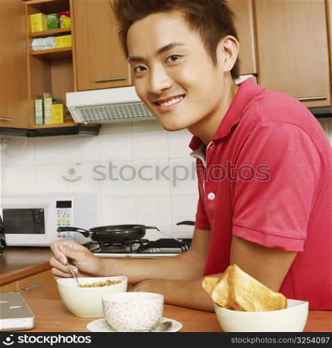 Portrait of a young man having breakfast in front of a laptop at a kitchen counter