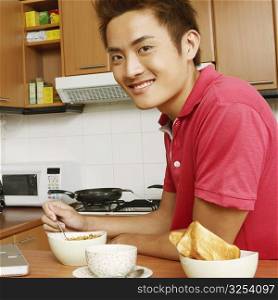 Portrait of a young man having breakfast in front of a laptop at a kitchen counter