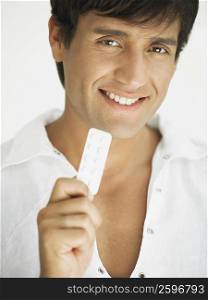 Portrait of a young man holding a blister pack and smiling