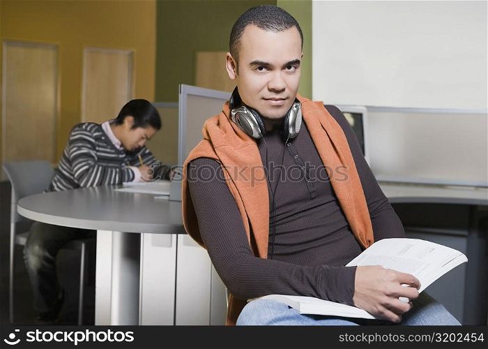 Portrait of a young man holding a book in a computer lab