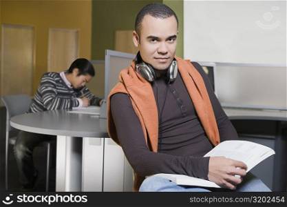 Portrait of a young man holding a book in a computer lab