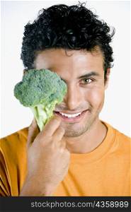 Portrait of a young man holding a broccoli in front of his face and smiling