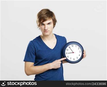 Portrait of a young man holding a clock over a gray background