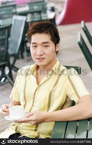 Portrait of a young man holding a coffee cup and a saucer