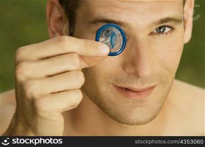 Portrait of a young man holding a condom in front of his eye