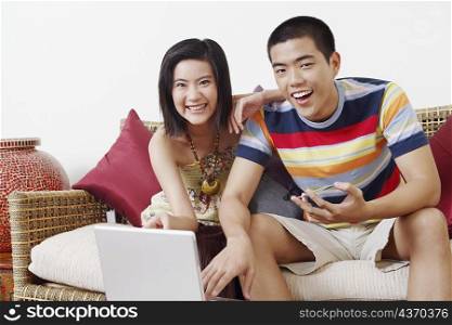 Portrait of a young man holding a credit card and using a laptop with a young woman sitting beside him