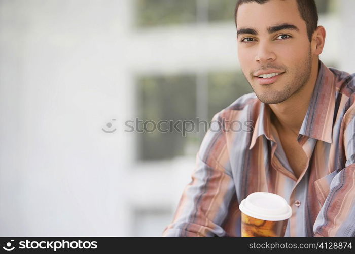 Portrait of a young man holding a cup of cold drink and smiling