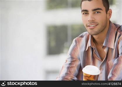 Portrait of a young man holding a cup of cold drink and smiling