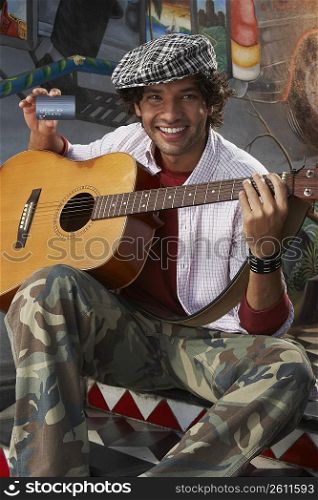 Portrait of a young man holding a guitar and a credit card