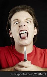 Portrait of a young man holding a knife up to his chin and sticking his tongue out