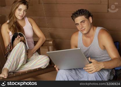 Portrait of a young man holding a laptop with a young woman sitting on a porch swing
