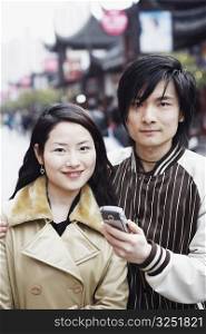 Portrait of a young man holding a mobile phone with a young woman smiling