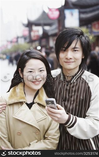 Portrait of a young man holding a mobile phone with a young woman smiling
