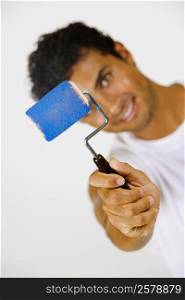 Portrait of a young man holding a paint roller and smiling