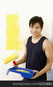 Portrait of a young man holding a paint roller with a paint tray and smiling